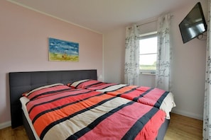 Ein Schlafzimmer mit Bett, einem Gemälde, einem Fernseher und einem Fenster mit Vorhängen.