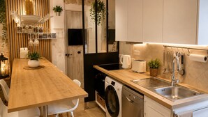A modern kitchen with a wooden table, white chairs, a washing machine, a dishwasher, and a sink. - 16624498LIONS Le Suquet Old Town Forville Cozy Apartment (Cannes)