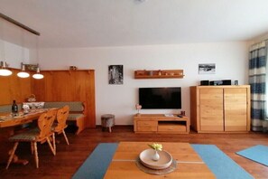 Ein Wohnzimmer mit Fernseher, Holzmöbeln und einem Essbereich mit Stühlen und Tisch.
