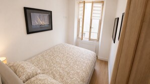 A bedroom with a bed, a window with blinds, a framed picture on the wall, and a door. - 16514416 LIONS La Croisette, just a stone's throw away (Cannes)