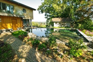 Ein Haus mit Schwimmbad, umgeben von Grünpflanzen und einem Steinhaus.