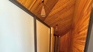 Käytävä, jonka seinät ja lattia ovat puupaneloituja, ja jossa on katosta roikkuva valaisin sekä ovikehys.