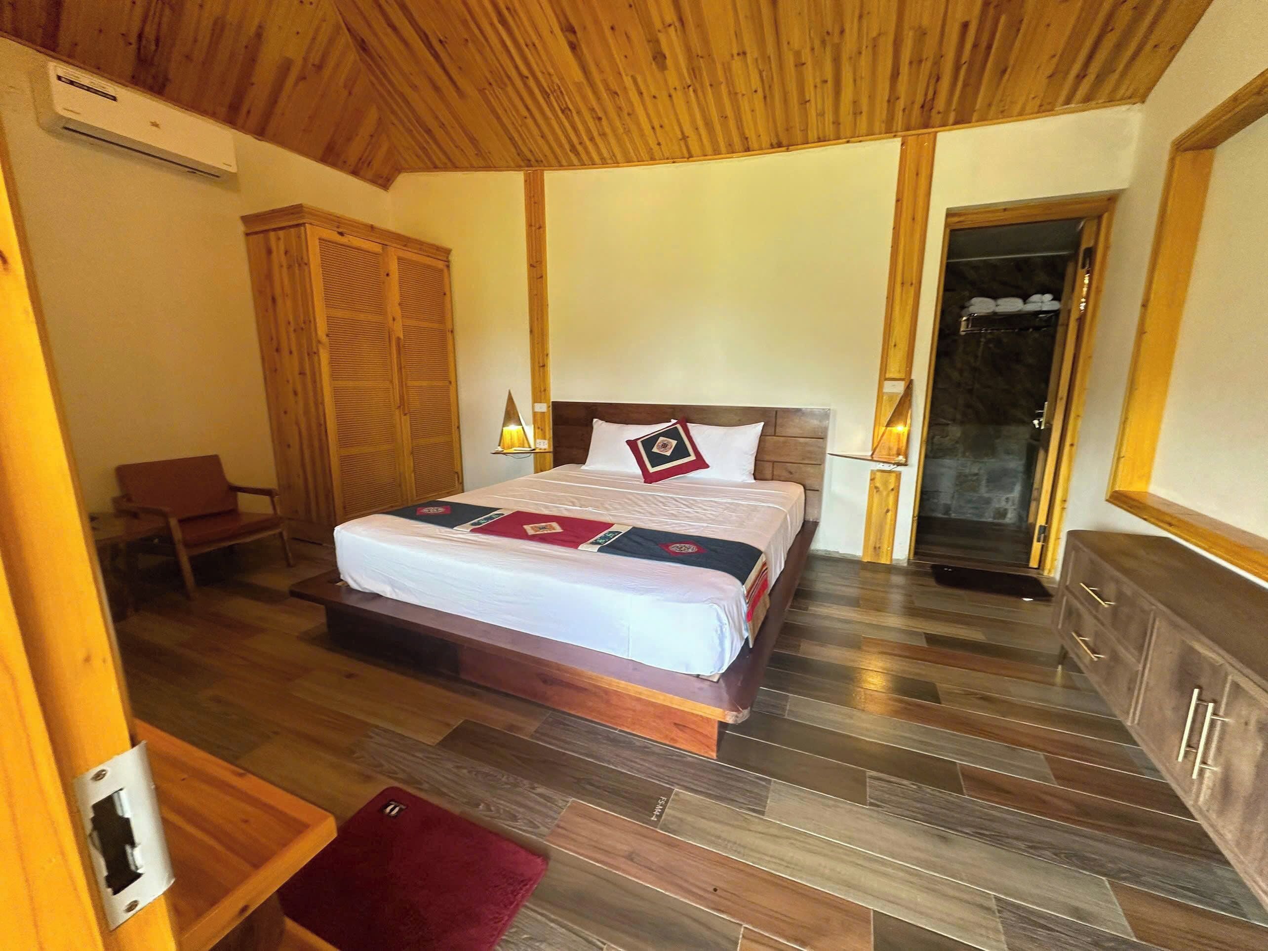 A bedroom with a wooden ceiling, a bed with a wooden headboard, a nightstand, a chair, a wardrobe, and a mirror.