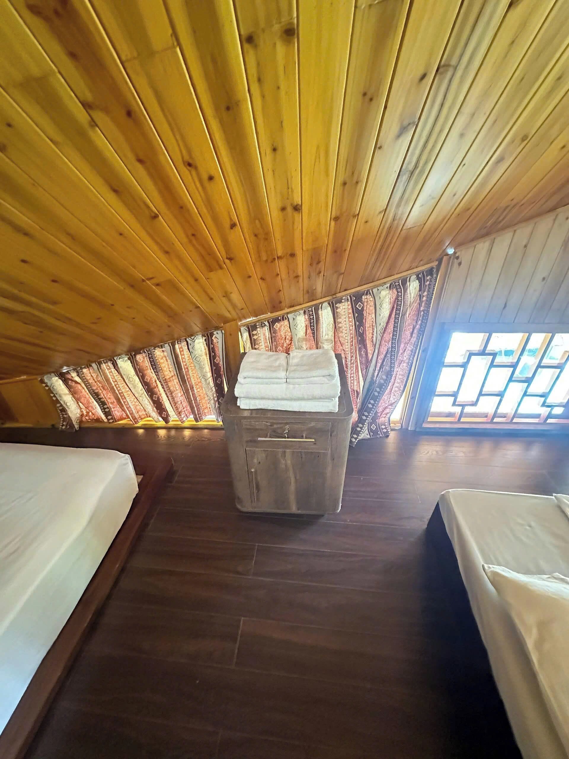 Quarto com teto de madeira, duas camas, um pequeno armário e cortinas estampadas.