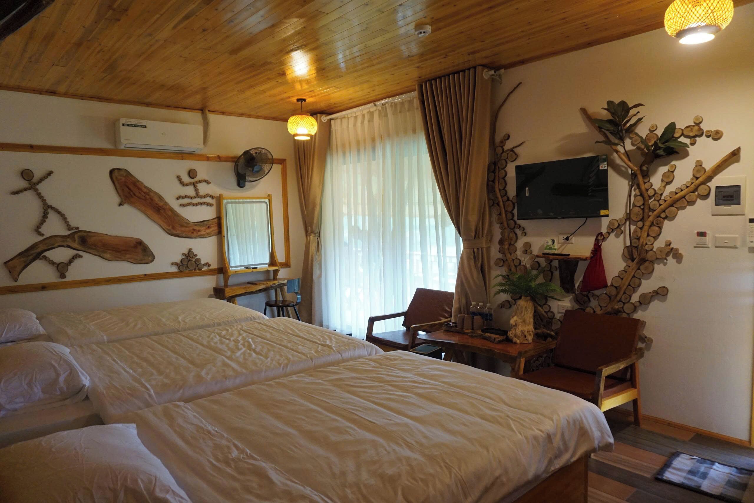 Habitación de hotel con techo de madera, cama con ropa blanca, escritorio con silla, televisor y planta en la pared.