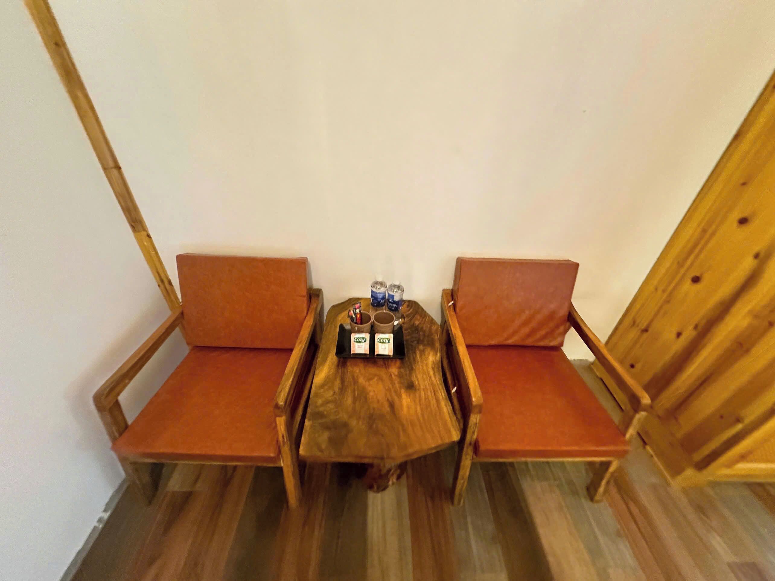 Ein Holztisch mit zwei gepolsterten Stühlen, einer kleinen Ablage mit Gegenständen und einer schlichten weißen Wand.