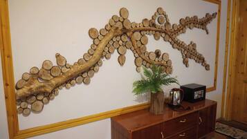 Una instalación artística en la pared hecha con piezas de madera, una pequeña planta en maceta y una cafetera sobre un mueble de madera.