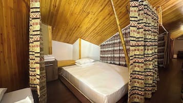 A room with a sloped ceiling, a bed with a white mattress, and patterned curtains.