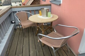 Ein Balkon mit Korbstühlen, einem Metalltisch und einem Metalleimer.