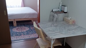 Una habitación con una cama, una mesa con sillas, un escritorio pequeño con lámpara y un radiador.