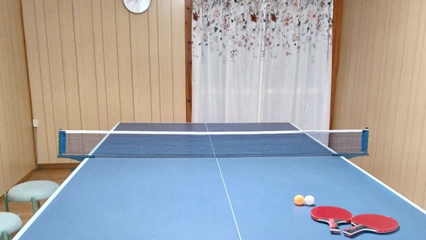 A ping pong table with two red paddles and two balls, a clock, and an air conditioner on the wall. - guest house mami (Taketa)