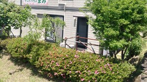 Un edificio de dos pisos con fachada de ladrillo, un letrero con caracteres japoneses y un jardín con flores rosadas.