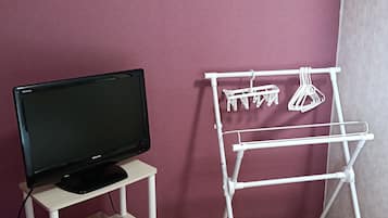 A room with a television on a stand, a white drying rack, a framed picture on the wall, and a clock on a shelf.