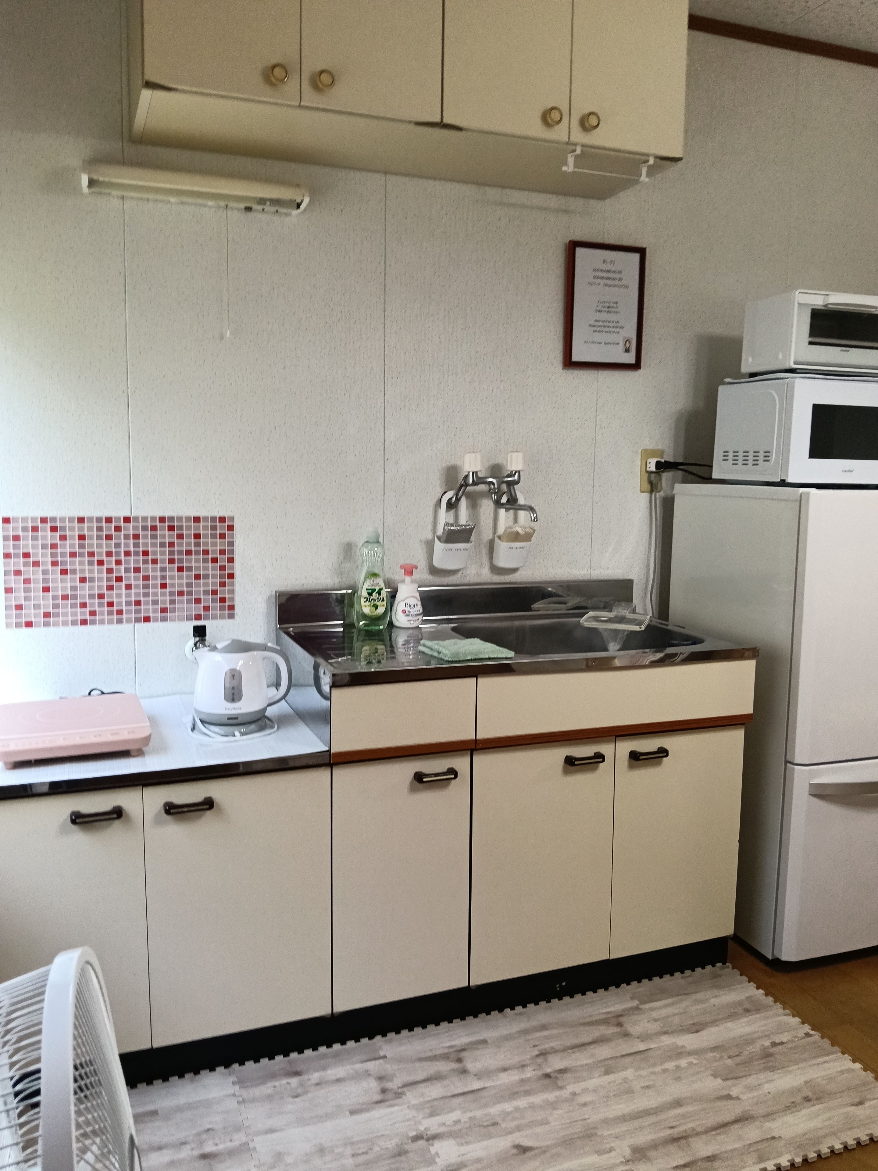 A kitchen with a microwave, kettle, and a pink electronic device on the counter.