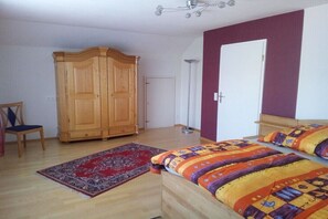 Ein Schlafzimmer mit einem Holzschrank, einem roten Teppich mit Muster, einem Bett mit farbenfroher Bettwäsche und einer Stehlampe.
