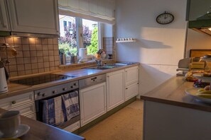 Eine Küche mit weißen Schränken, einem Fenster, einer Uhr und einem Spülbecken.