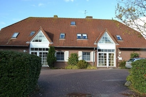 A two-story building with a red-tiled roof, a central entrance with glass doors, and a small window on the upper floor. - Greetsieler Scholle 1 - Holiday apartment (Greetsiel)