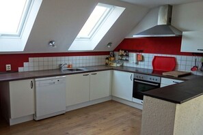 Eine Küche mit Oberlicht, weißen Schränken, einem Geschirrspüler, einem Backofen und einer roten Akzentwand.