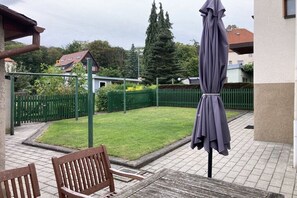 Eine Terrasse mit einer Bank, einem Sonnenschirm und einem grünen Zaun.