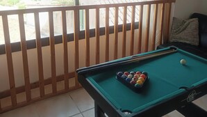 Ein Billardtisch mit Kugeln, ein Fenster mit Blick auf grüne Hügel und ein Balkongeländer.
