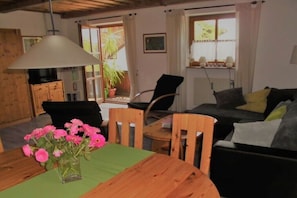Ein Wohnzimmer mit Esstisch, Stühlen, einer Couch, einer Lampe und einem Blumentopf.
