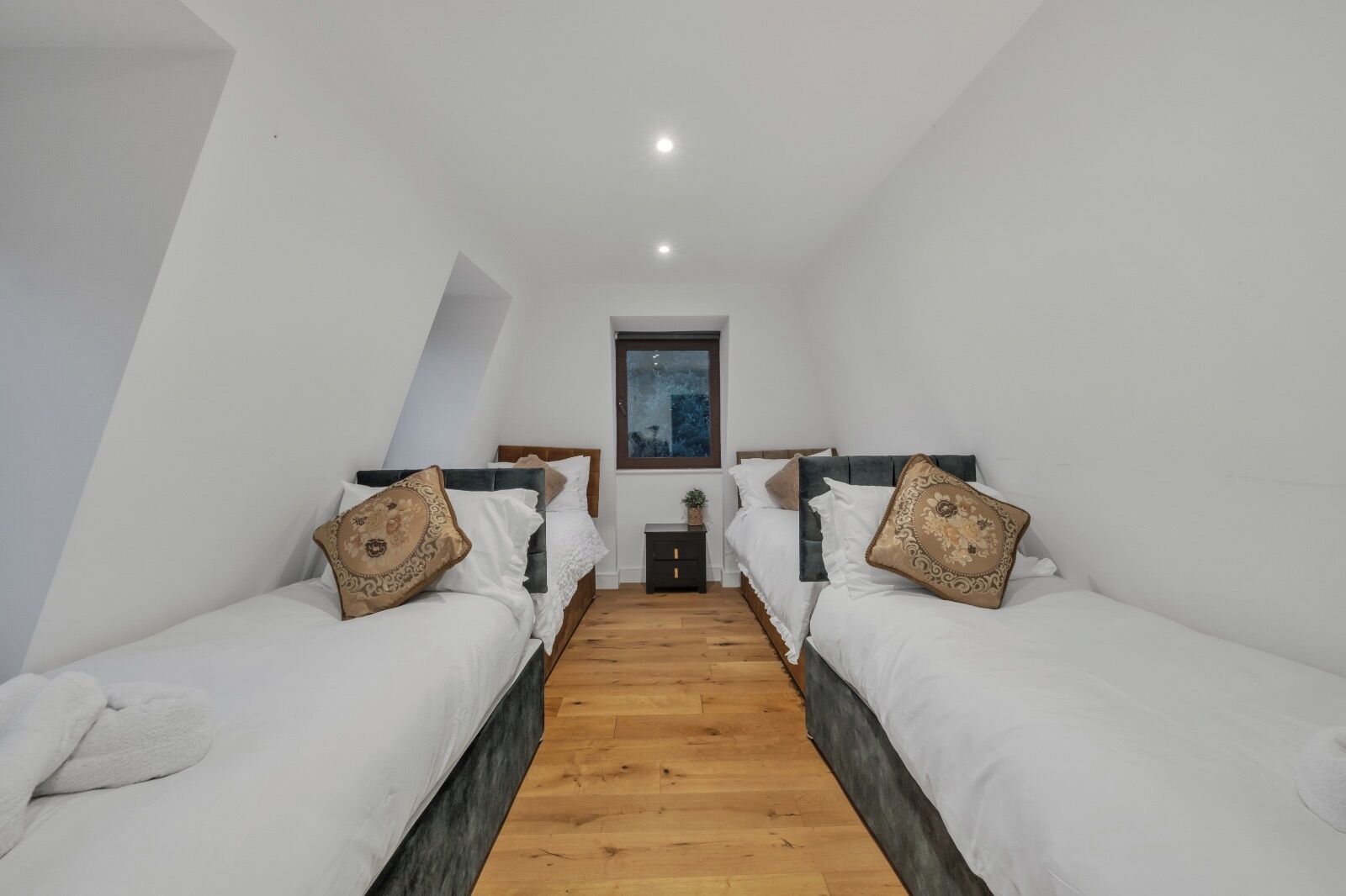 Ein Schlafzimmer mit zwei Betten, Holzboden, einem kleinen Nachttisch und einem Fenster.