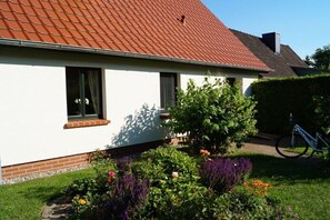 Ein Haus mit rotem Ziegeldach, einem Backsteinfundament und einem Garten mit verschiedenen Pflanzen und Blumen.