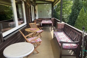 Een overdekt terras met houten meubels en een bakstenen muur.
