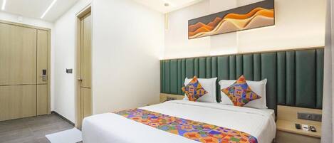Una habitación de hotel con una cama, cabecero, una obra de arte en la pared, mesita de noche y armario.