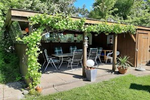 Eine Holz-Pergola mit Tisch und Stühlen, umgeben von viel Grün.