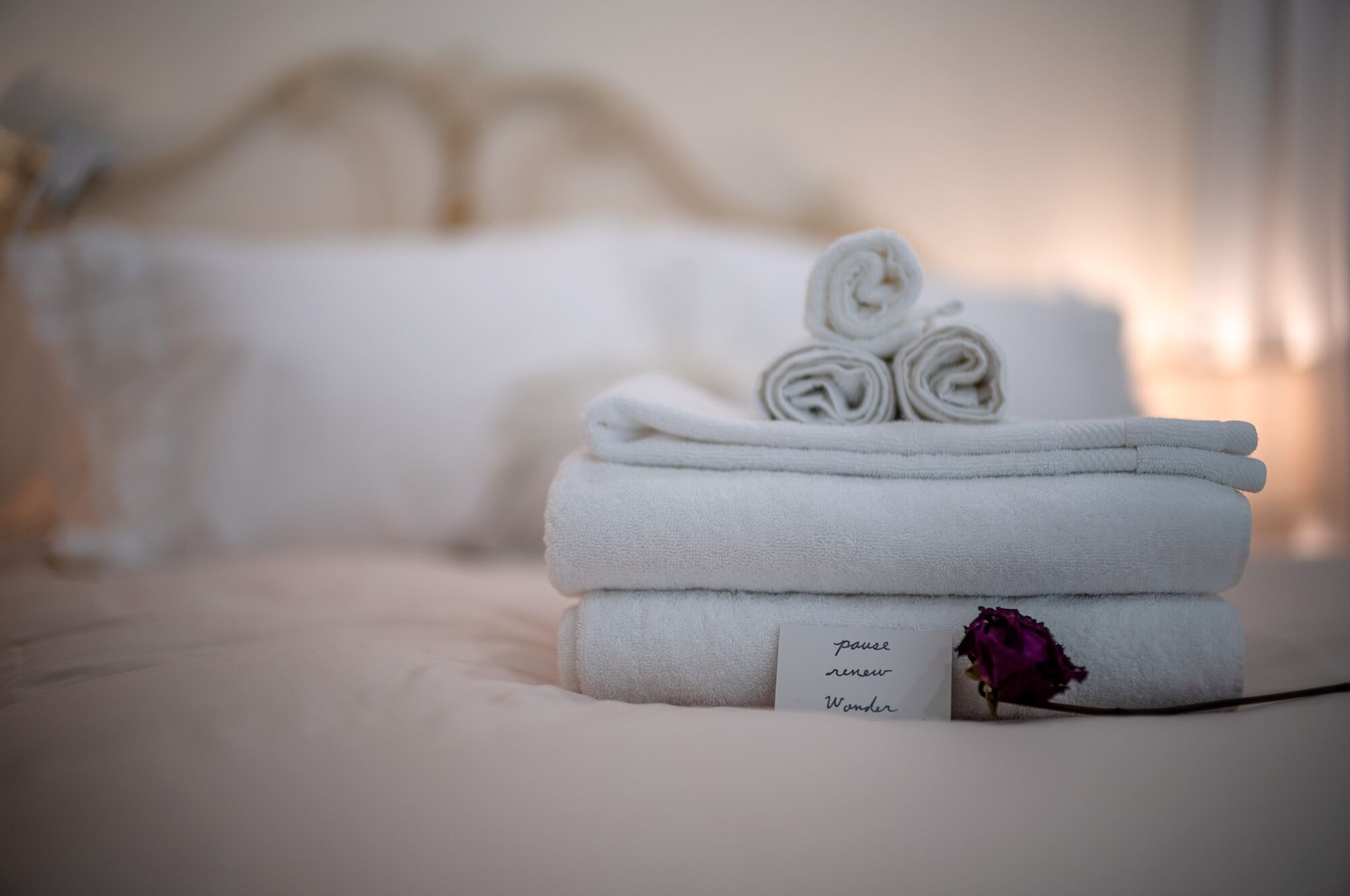 Une pile de serviettes blanches, soigneusement pliées, est posée sur le lit, et une étiquette indique : « Faites une pause, ressourcez-vous, retrouvez l’émerveillement. »
