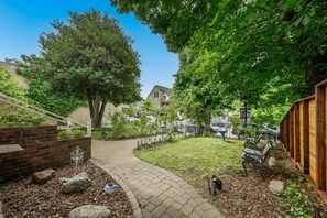 A garden pathway leading to a bench, surrounded by trees and a brick wall. - Holly House, your Portal to Mt. Shasta Bliss. (Mount Shasta)
