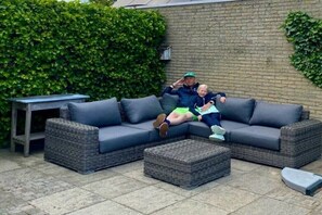 A sectional sofa with a matching ottoman, a small table, and a hedge in the background. - Holiday home in Koudum with swimming pool (Koudum)