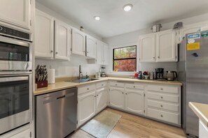 A modern kitchen with stainless steel appliances, white cabinetry, and a window with autumn foliage. - The Hemlock House | The Disconnect Cabin (Dunsmuir)