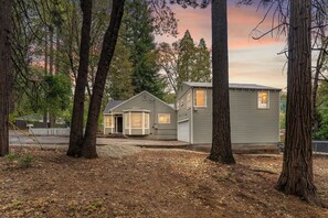 A two-story house with a front porch, surrounded by trees and a white picket fence. - The Hemlock House | The Disconnect Cabin (Dunsmuir)