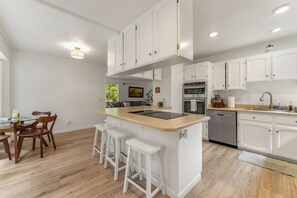 A modern kitchen with white cabinetry, a central island with stools, and built-in appliances. - The Hemlock House | The Disconnect Cabin (Dunsmuir)