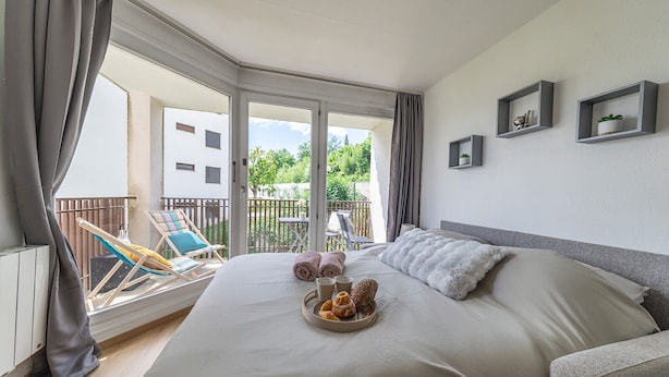 Un dormitorio con una cama grande, un balcón con una silla y vistas a zonas verdes.