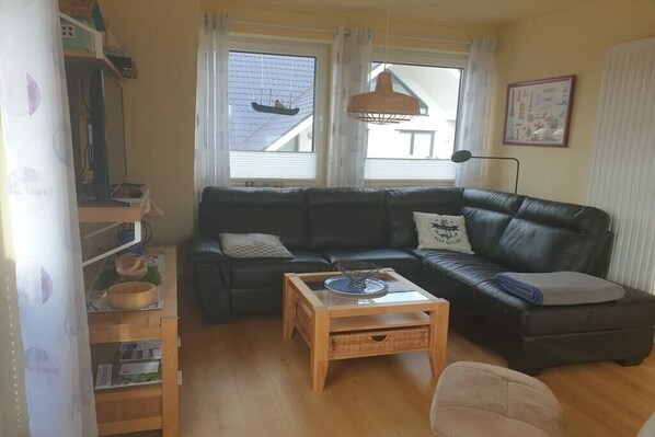 A living room with a black leather sofa, a wooden coffee table, and a bookshelf. - Lighthouse on the sandy beach (Niedersachsen - Norden)