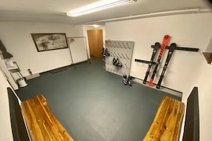 Ein Zimmer mit grauem Boden, Holzbanken, einem Skiständer und einer Tür.