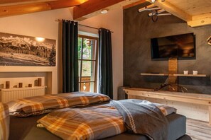 Ein Schlafzimmer mit zwei Betten, einem an der Wand befestigten Fernseher, einem Fenster mit Vorhängen und einer Heizung.
