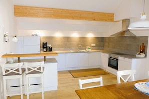 Una cocina moderna con armarios blancos, encimera de madera, horno empotrado y una lámpara colgante.