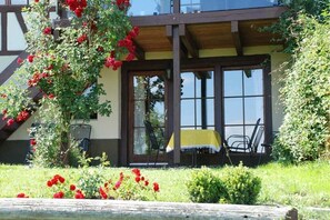 Ein Gebäude mit einem großen Fenster, einer Holztreppe und einem Garten mit roten Blüten.