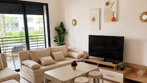 A modern living room with a sofa, a coffee table, a TV, and a balcony with a view.