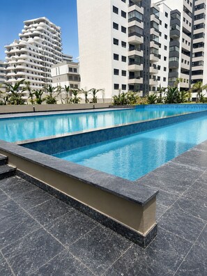 Una piscina con borde de azulejos, rodeada de un área ajardinada con palmeras.