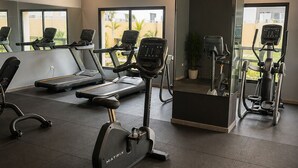 A gym with treadmills, an elliptical, and a stationary bike, with large windows and a potted plant.
