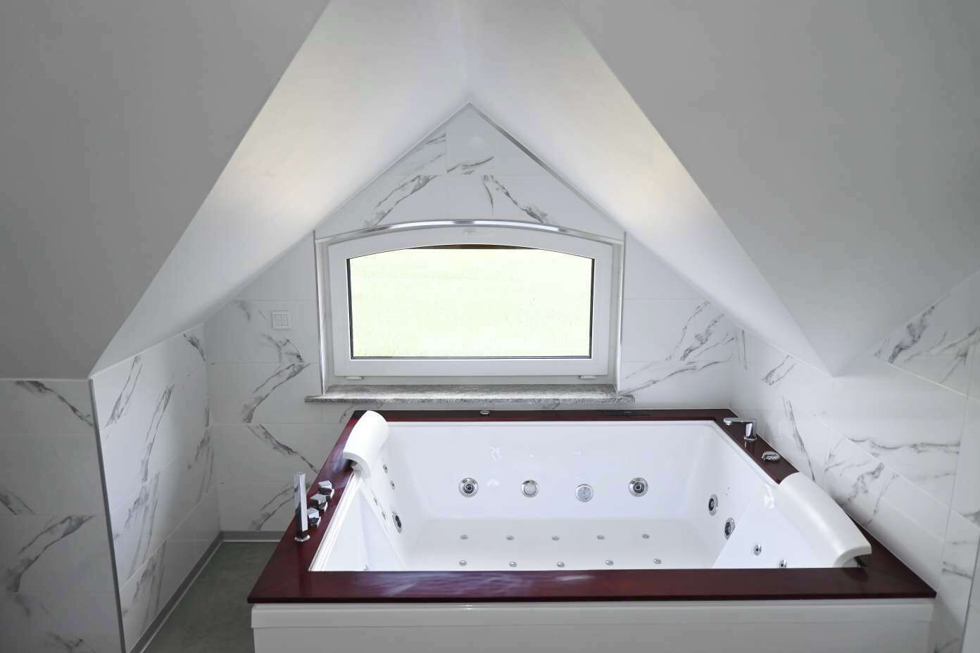 Ein Badezimmer mit freistehender Badewanne, einem Fenster und Marmorwänden.