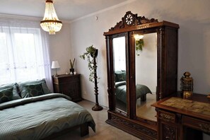 Un dormitorio con un espejo grande, una cama con ropa de cama verde, una lámpara de pie y un aparador.