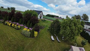 Ein Haus mit schrägem Dach, umgeben von gepflegten Gärten und Bäumen.