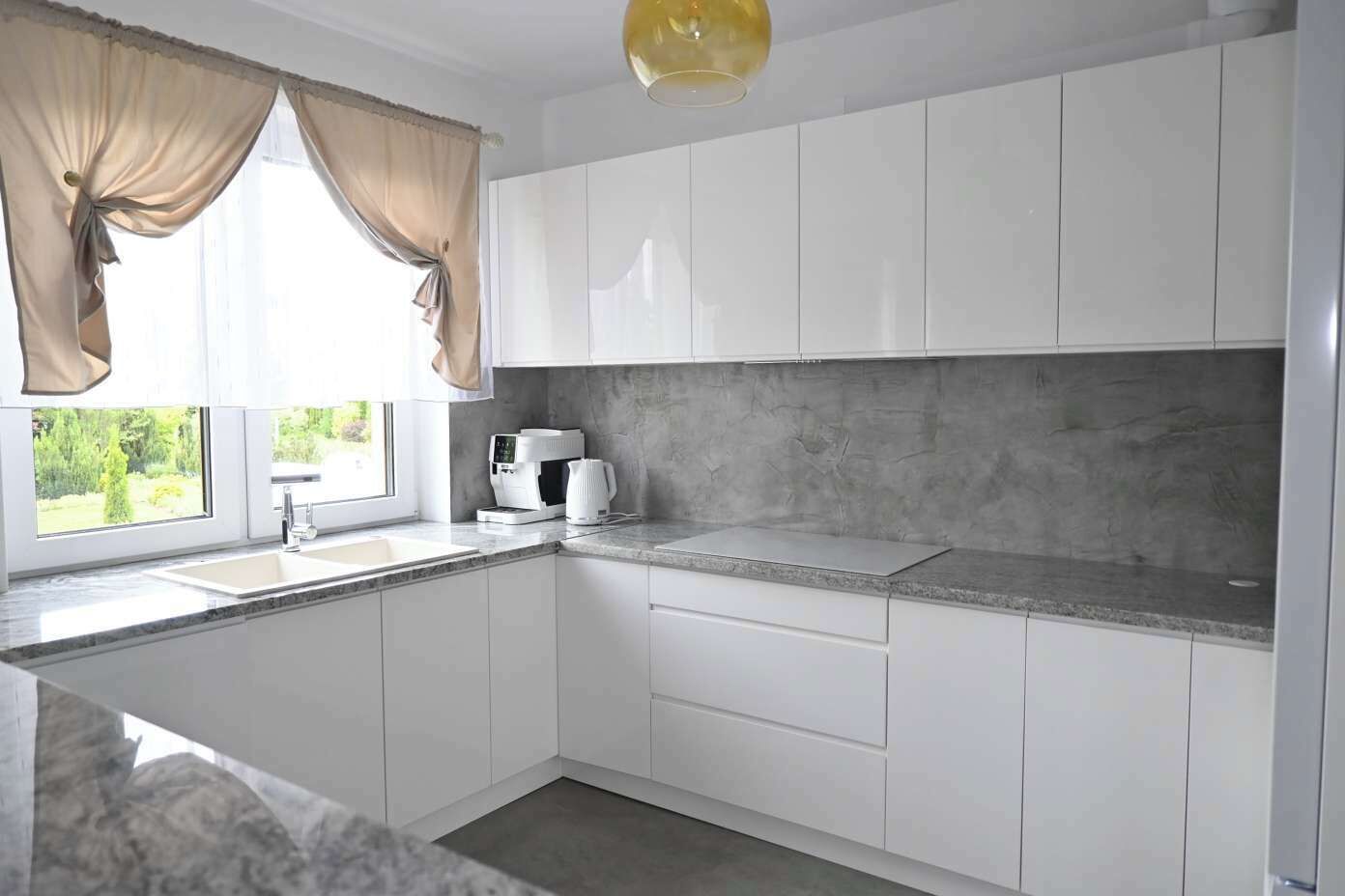 Une cuisine moderne avec des meubles blancs, un plan de travail en granit, une machine à café et une vue sur la verdure à l’extérieur.