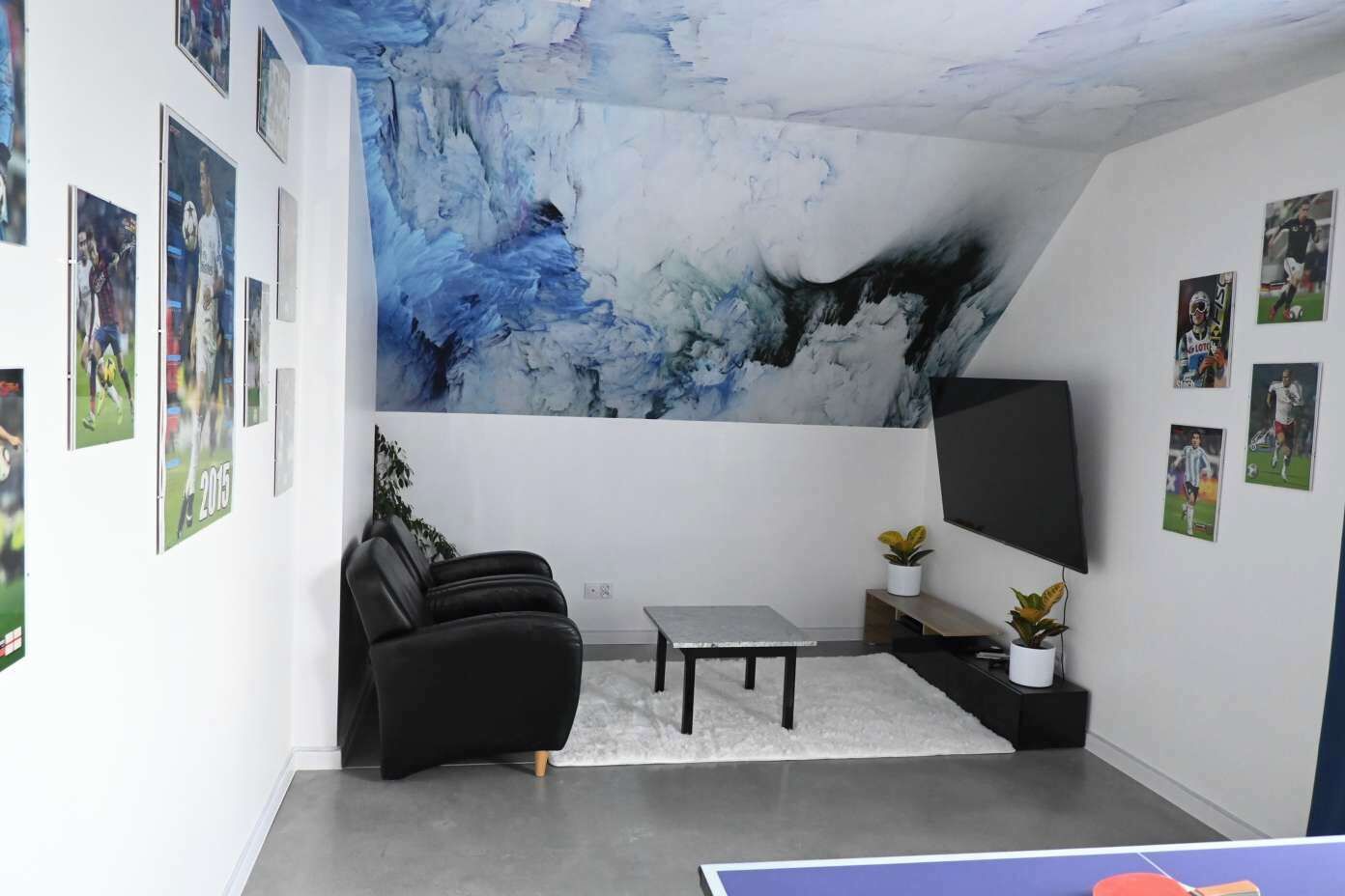 Ett rum med en stor, abstrakt väggmålning, en platt-TV, en soffa, ett soffbord och sportrelaterade minnessaker på väggarna.